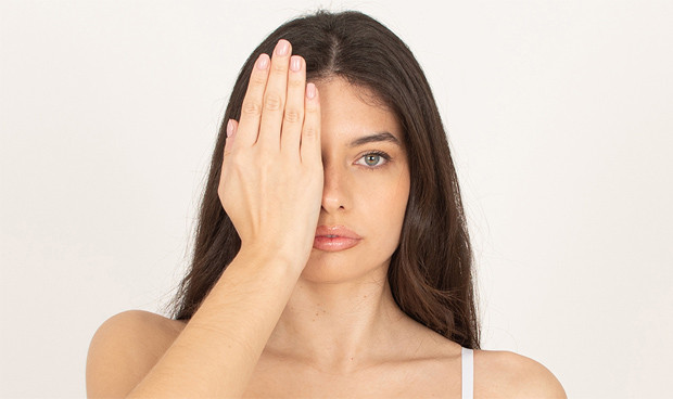 Mujer joven se cubre un ojo para una evaluación visual, gesto habitual previo a una cirugía de blefaroplastia.
