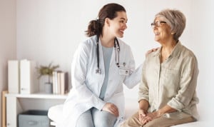 Doctora joven sonriendo y conversando con una paciente mayor durante una consulta médica en un entorno sanitario cercano y profesional.