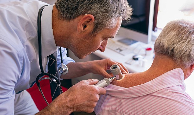 Dermatólogo examina a paciente mayor con dermatoscopia en la clínica