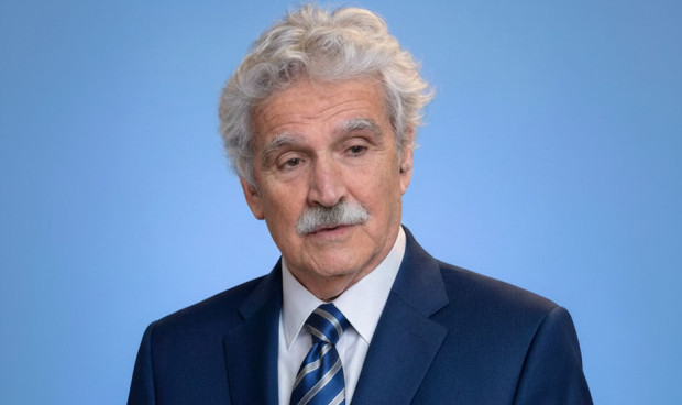 Un hombre mayor, con pelo y bigote blancos, posa en traje con corbata