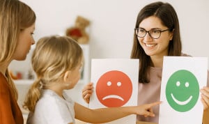 Psicóloga infantil muestra tarjetas emocionales a una niña en sesión terapéutica, acompañada por su madre, en un entorno clínico cálido y profesional.