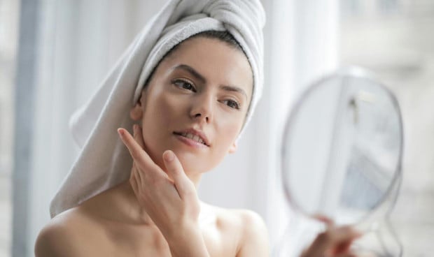 Mujer con toalla en la cabeza aplicándose crema facial, simbolizando el cuidado diario de la piel y la hidratación tras la limpieza.