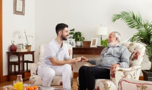Profesional sanitario de Sanitas conversa y entrega medicación a un hombre mayor en su hogar, fomentando el cuidado personalizado y la autonomía.