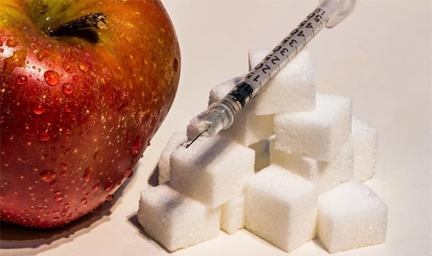 Manzana junto a terrones de azúcar con una jeringuilla encima